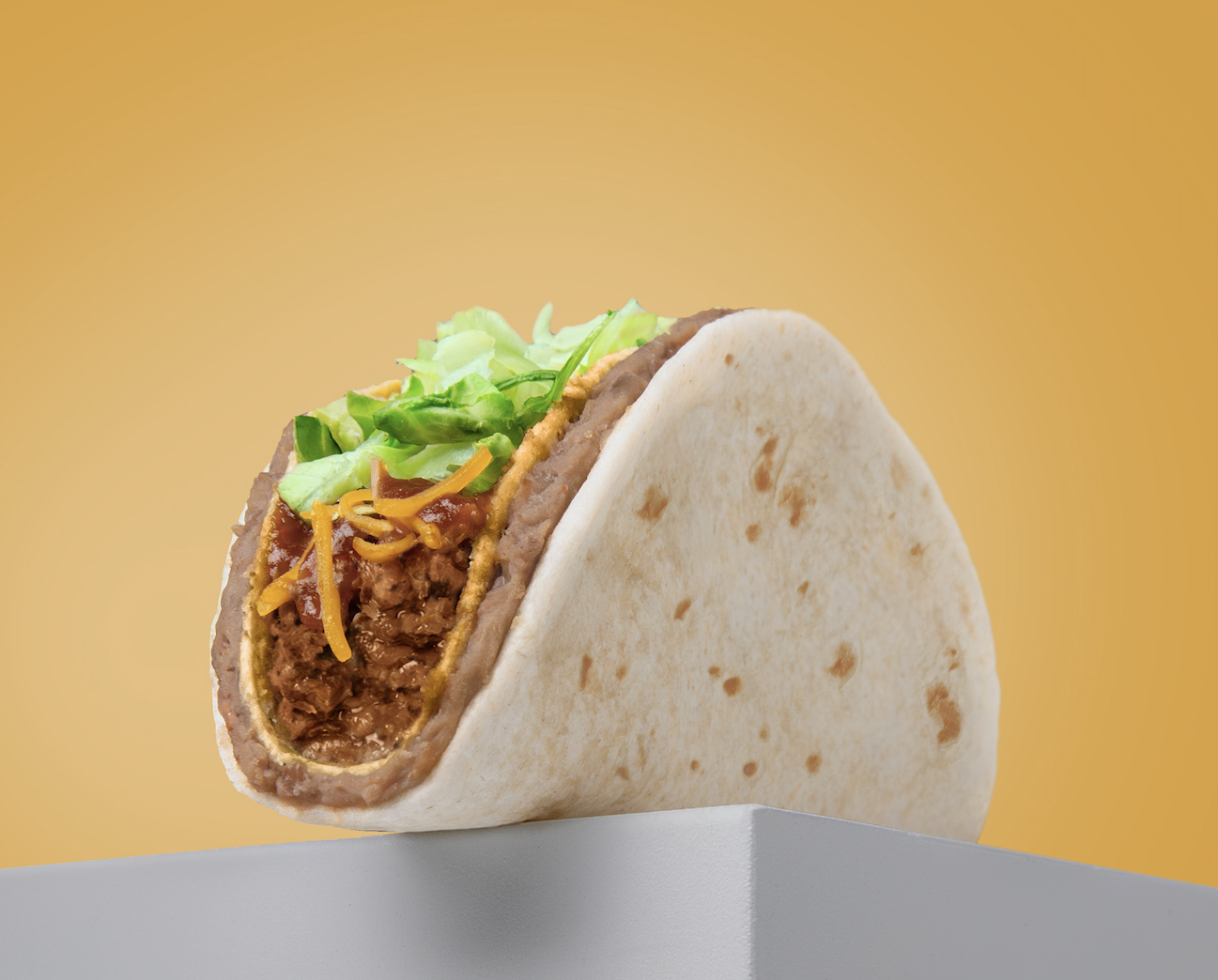 Our Taco Bravo a warm flour tortilla with a layer of refried beans wrapped around a crispy taco shell filled with 100% North American beef, Cheddar cheese, taco sauce, and shredded lettuce.